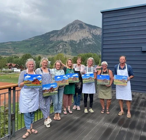 A group displaying vibrant mountain and floral landscapes that they painted at Beth Zink's painting class.